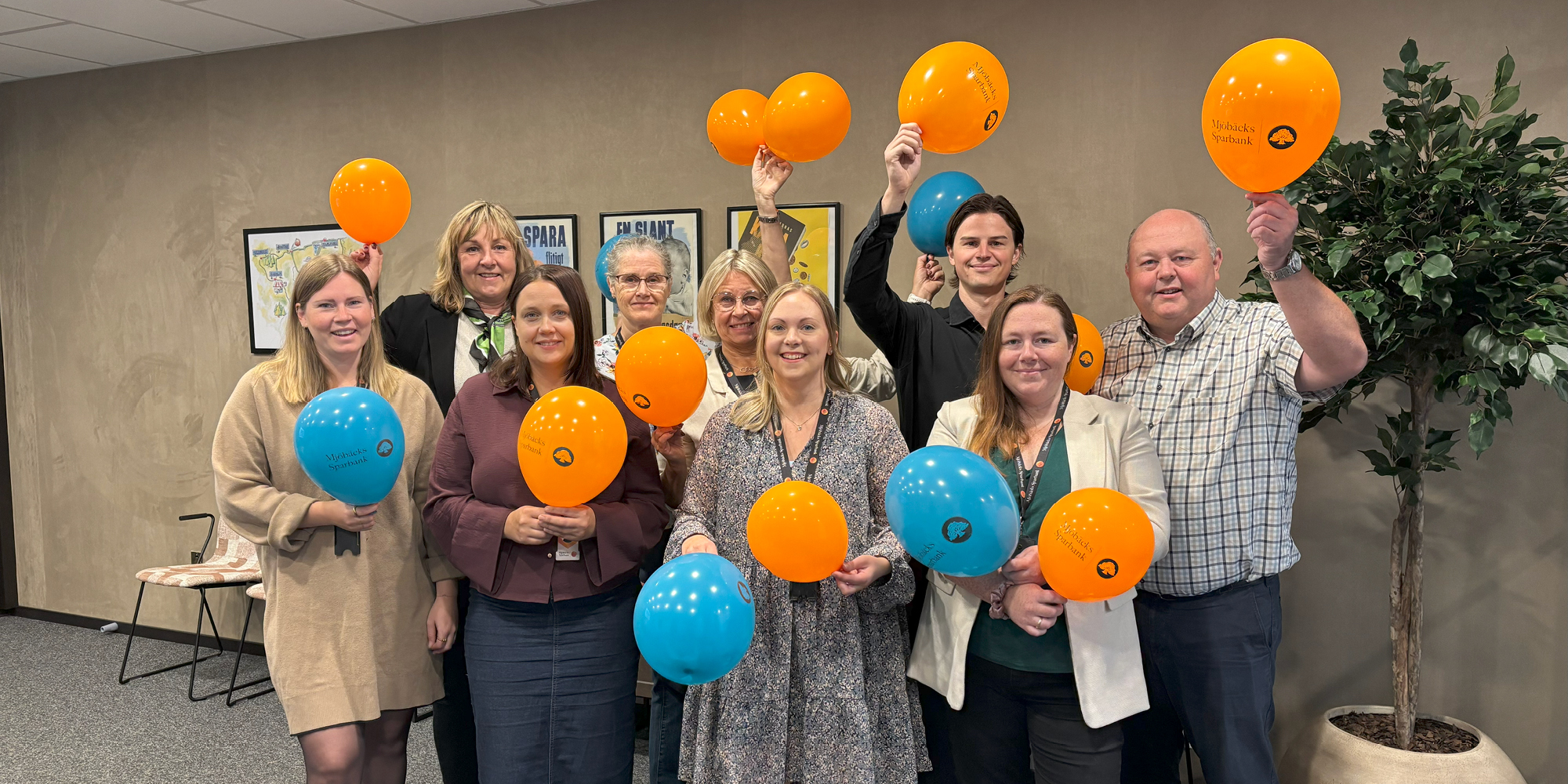 Gruppbild på glad personal som står inne och viftar med ballonger