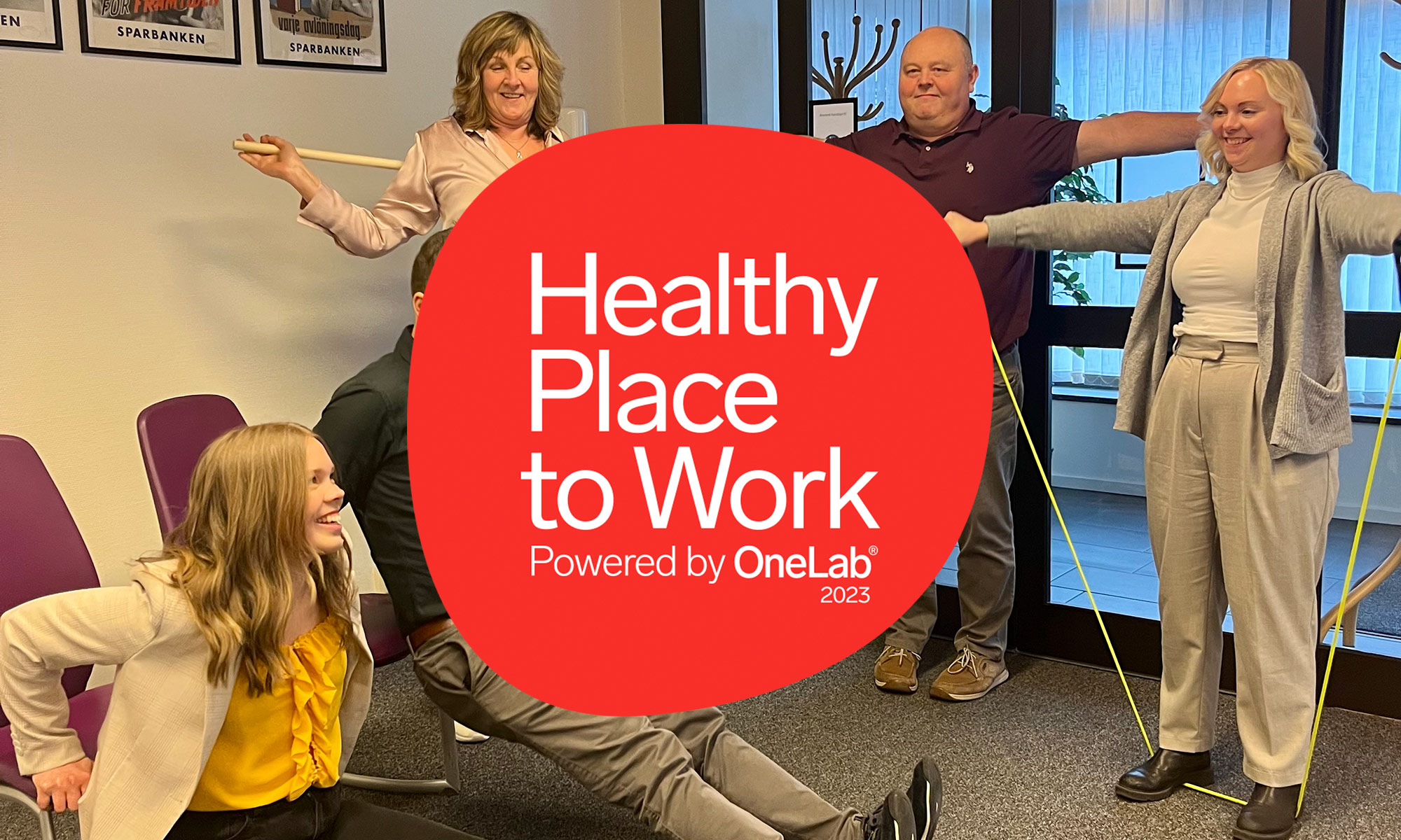 Logo with text: Healthy Place to Work Powered by OneLab 2023. People exercising in the background.